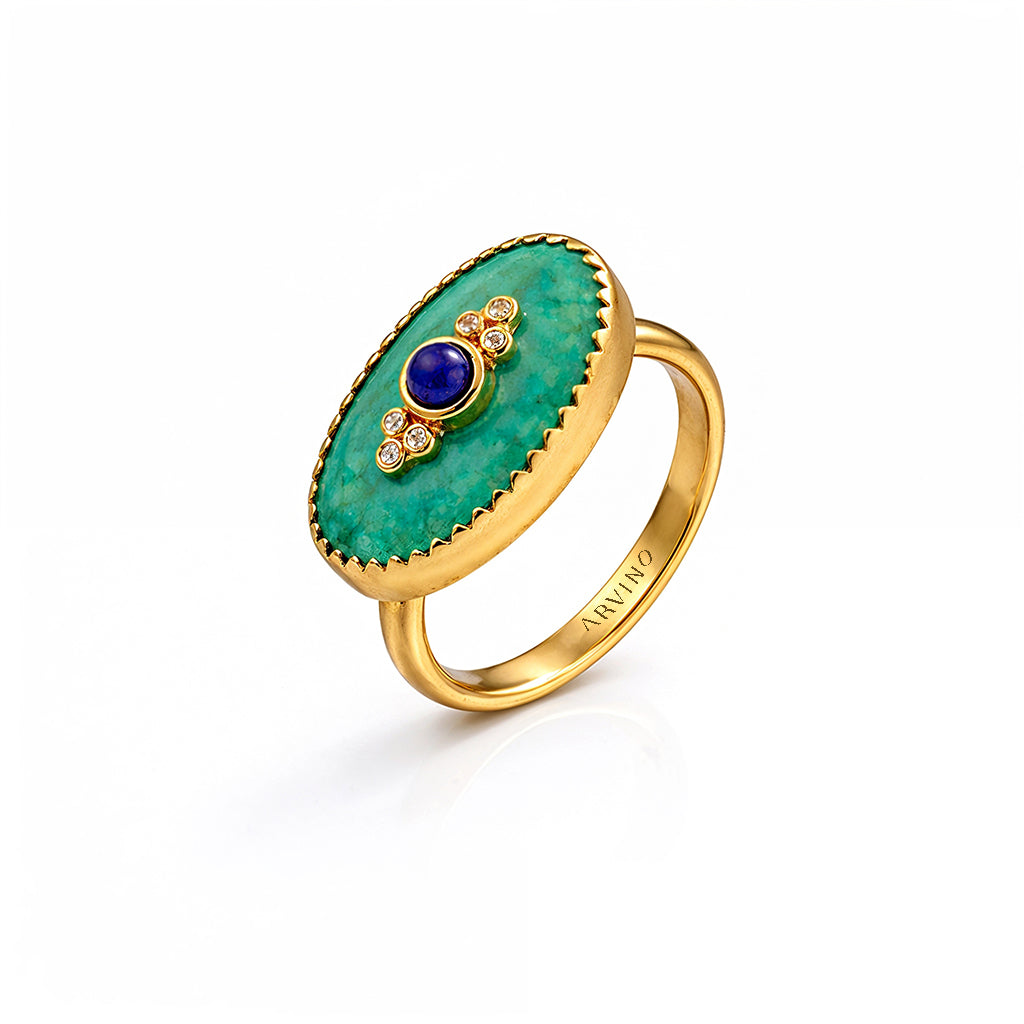 Gold ring with green gemstone and blue center on a white background