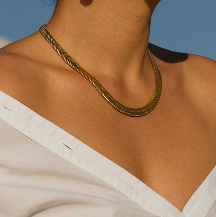 Woman wearing gold earrings and necklace against a clear blue sky