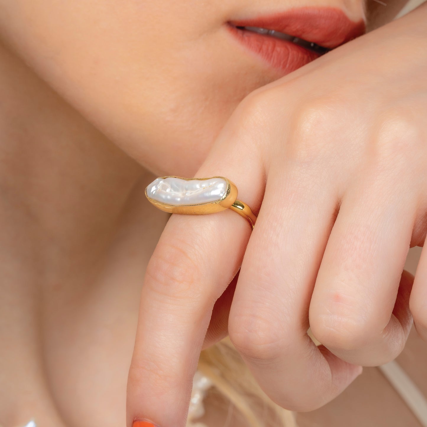 A close-up image of a person's hand showcasing a gold plated ring with a large baroque pearl centered on the finger.