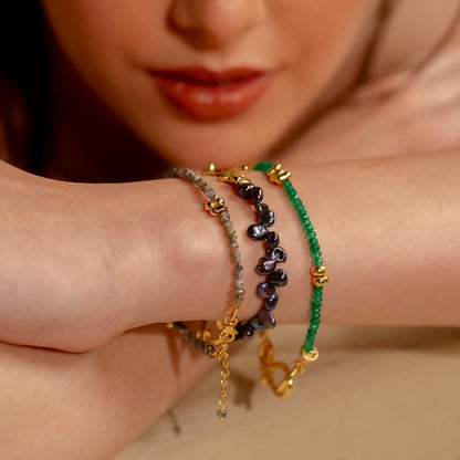 A close-up image of a person's wrist wearing a multi-strand bracelet with black pearls.