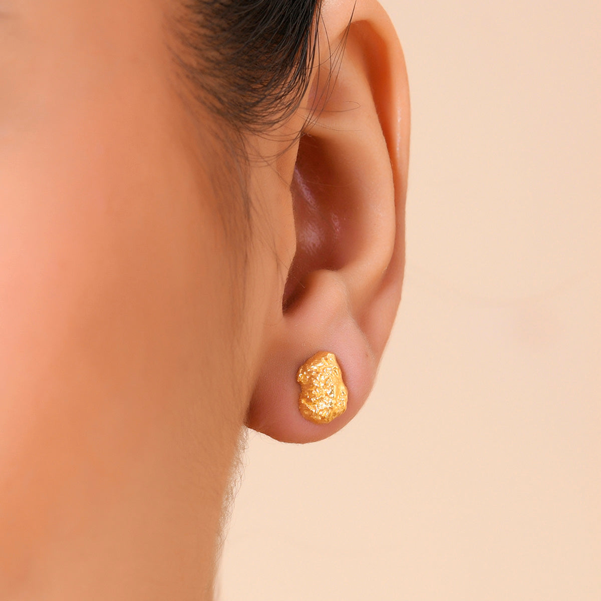 A close-up image of a person's ear wearing a gold-plated cobblestone textured stud earring.