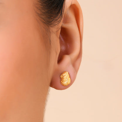 A close-up image of a person's ear wearing a gold-plated cobblestone textured stud earring.