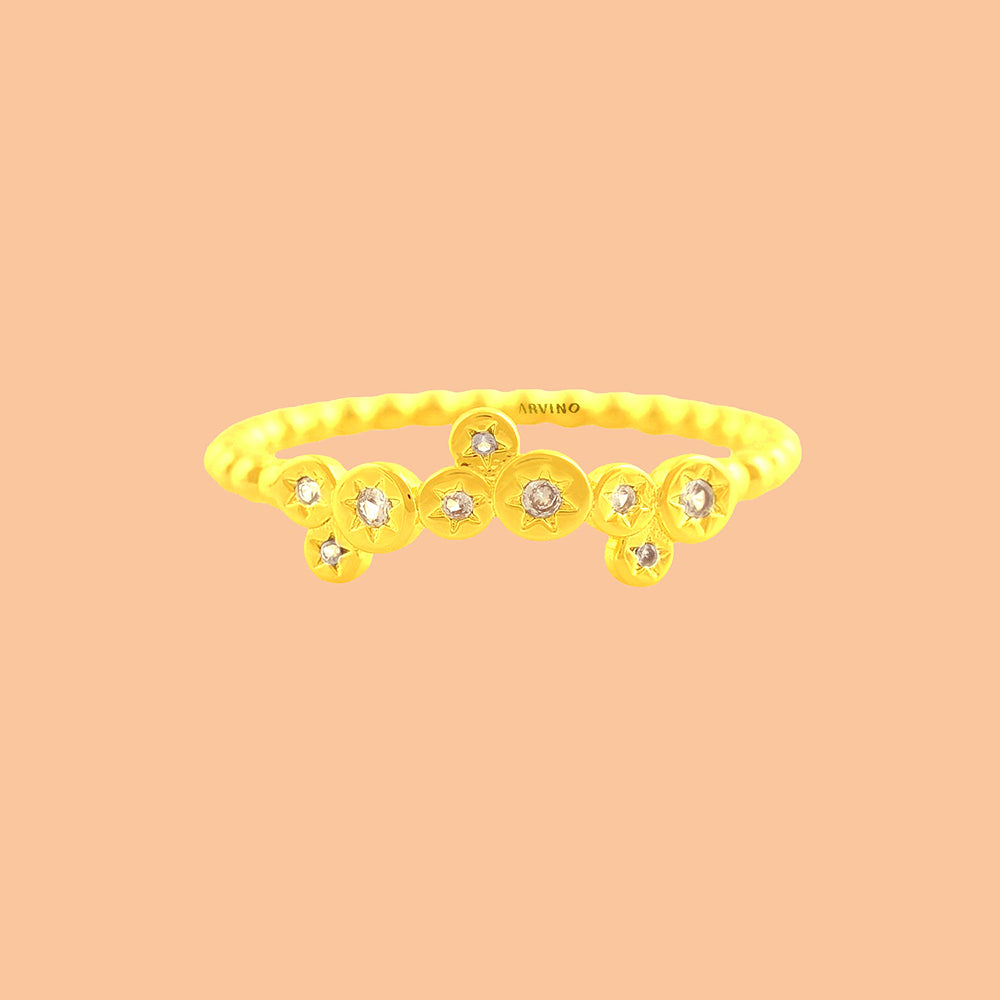 Minimal gold-toned stacking ring featuring star-engraved discs with clear stones, shown on a solid peach backdrop
