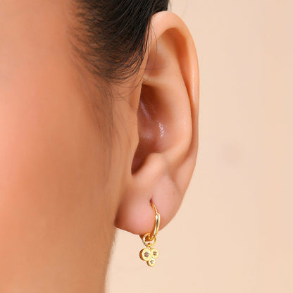 A close-up image of a person's ear wearing a gold-colored hoop earring with dangling crystals.