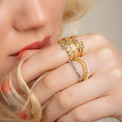 A person wearing multiple bands of gold and silver rings, featuring intricate designs and adorned with crystals.