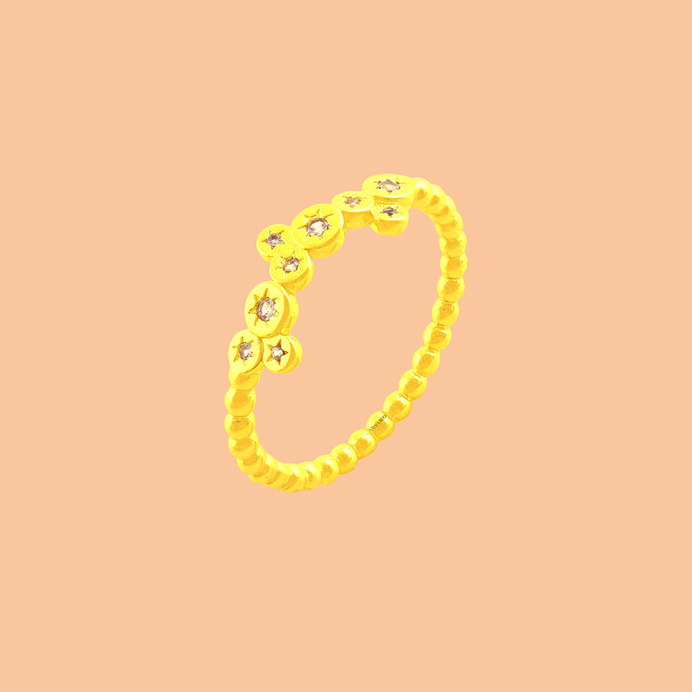 Minimal gold-toned stacking ring featuring star-engraved discs with clear stones, shown on a solid peach backdrop