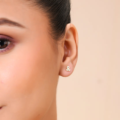 A close-up image of a person's ear wearing a single gold-colored stud earring with a triple crystal bezel.