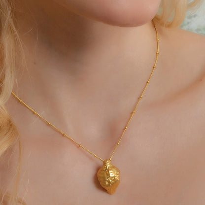 A person wearing a gold-colored sterling silver necklace with a leaf-shaped pendant.