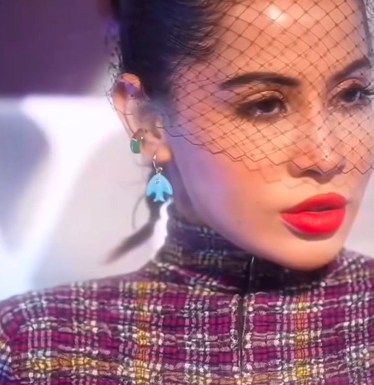 A close-up image of a person wearing turquoise fish motif earrings by Arvino.