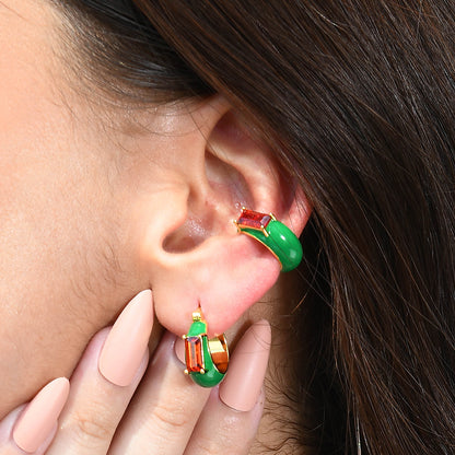 A person wearing a pair of green and red garnet enamel huggies as earrings.