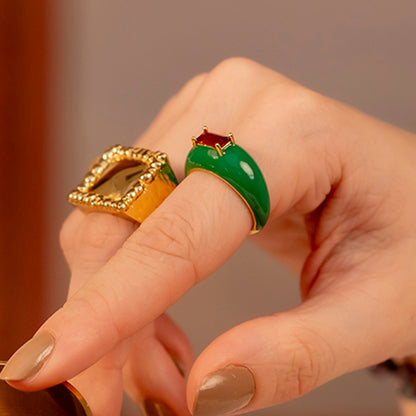 A hand wearing a vibrant green and gold-plated ring with a central garnet gemstone.