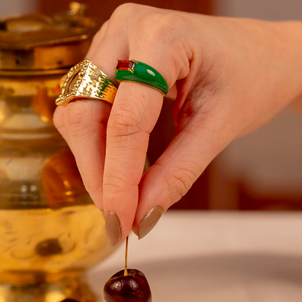 A hand wearing a vibrant green and gold-plated ring with a central garnet gemstone.