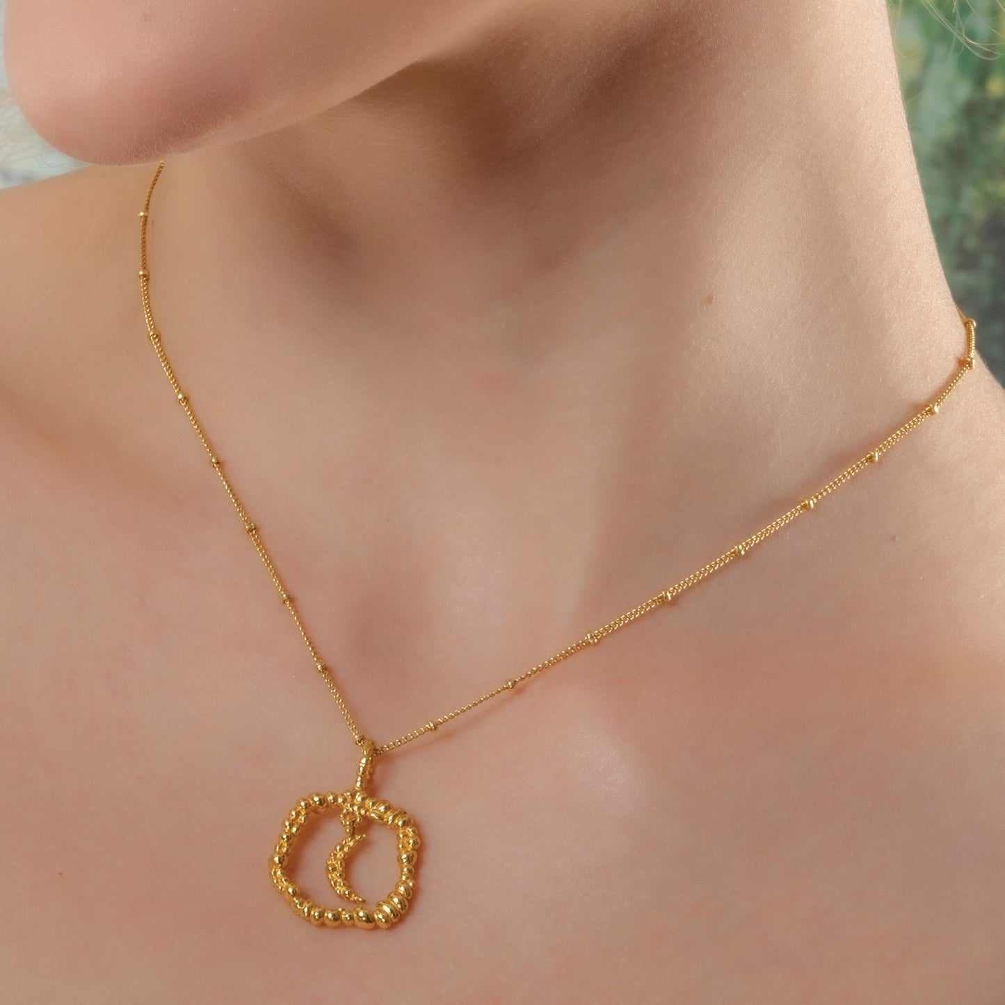 A person wearing a gold-colored necklace with a granulated texture circle pendant. Crescent moon necklace by Arvino