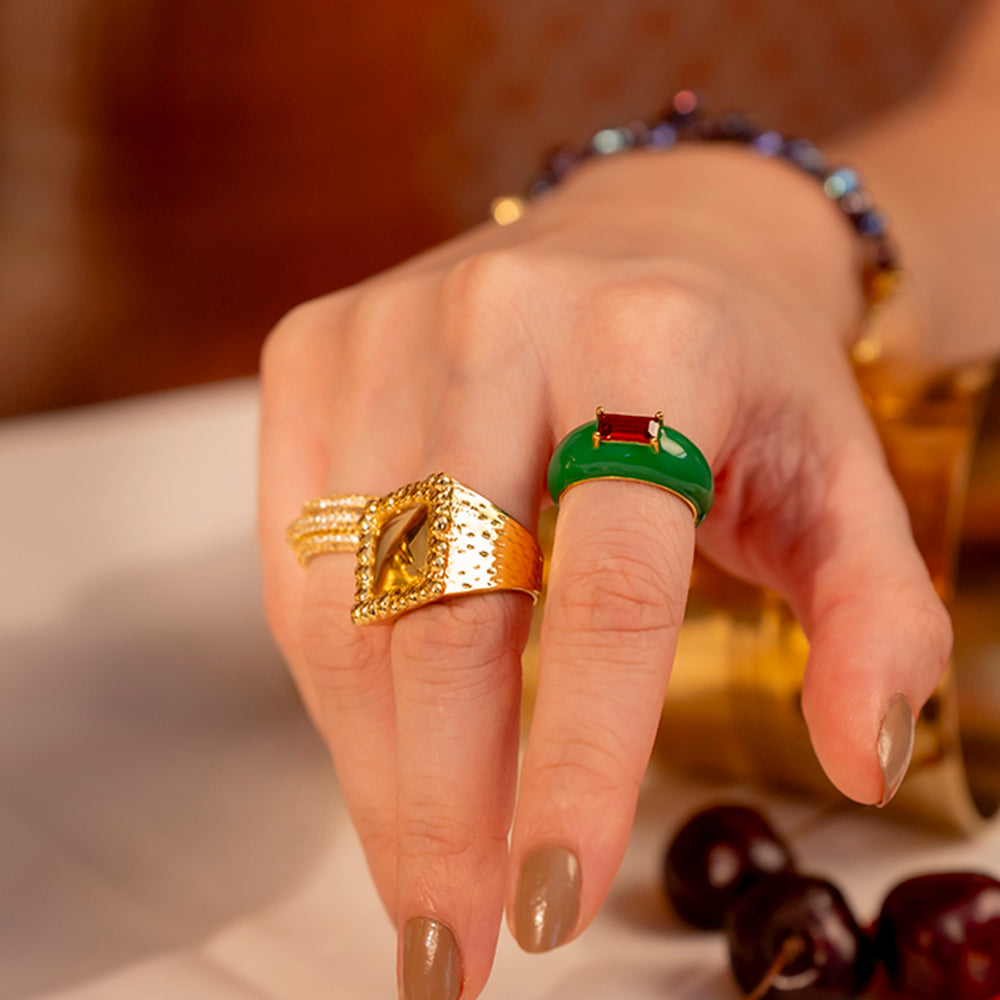A hand wearing a vibrant green and gold-plated ring with a central garnet gemstone.
