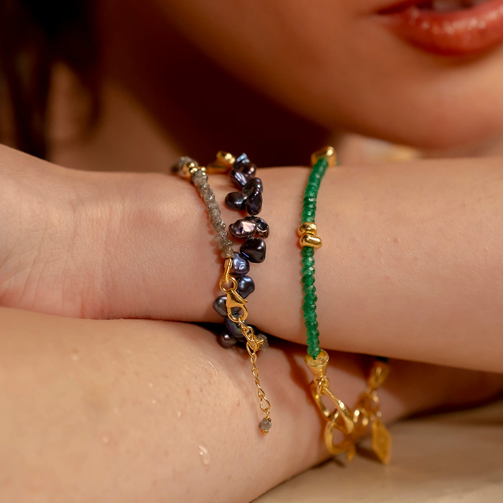 A person wearing multiple bracelets, featuring a mix of vibrant green and gold colors with various designs and gemstones.
