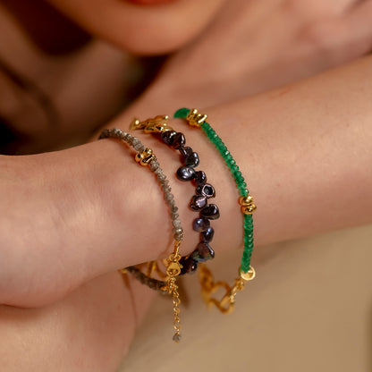 A person wearing multiple bracelets featuring black and Green beads with gold accents.