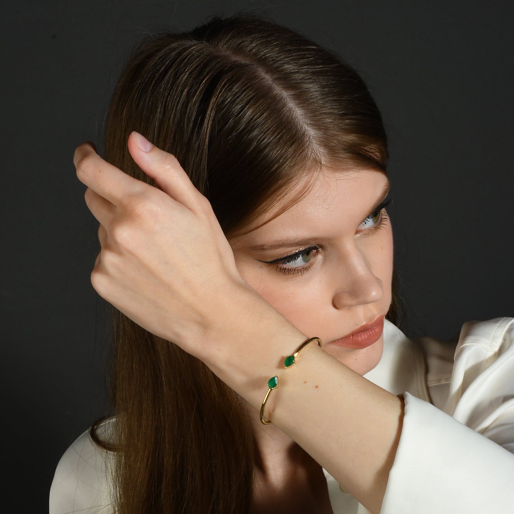 A person wearing a green onyx cuff bracelet with a sleek gold cuff, showcasing the deep green hue of the onyx against the gold metal.