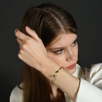 A person wearing a green onyx cuff bracelet with a sleek gold cuff, showcasing the deep green hue of the onyx against the gold metal.