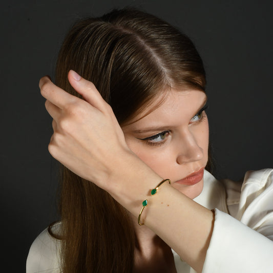 A person wearing a green onyx cuff bracelet with a sleek gold cuff, showcasing the deep green hue of the onyx against the gold metal.