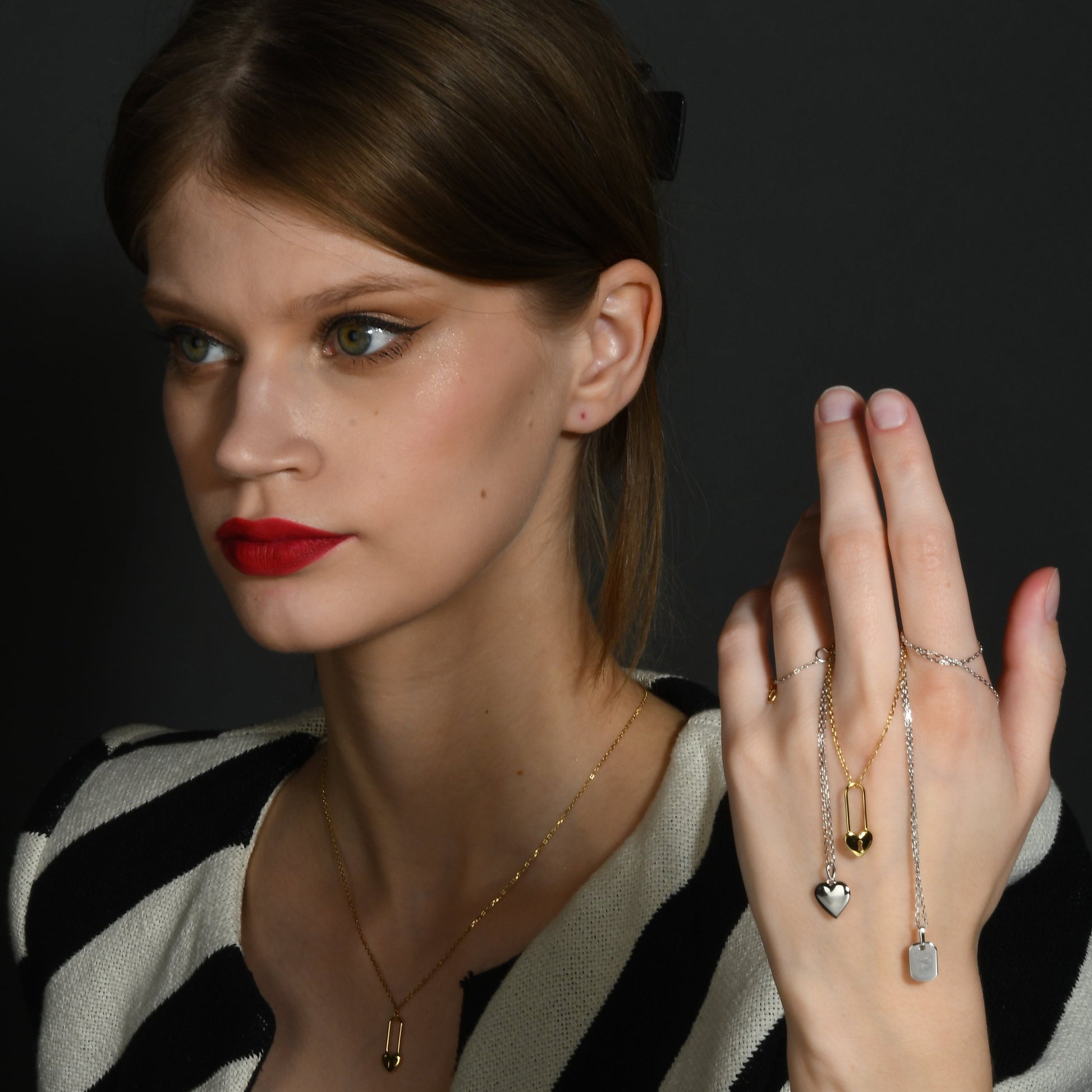 Model showcasing multiple necklace in hand with heart charm and lock charm on hand