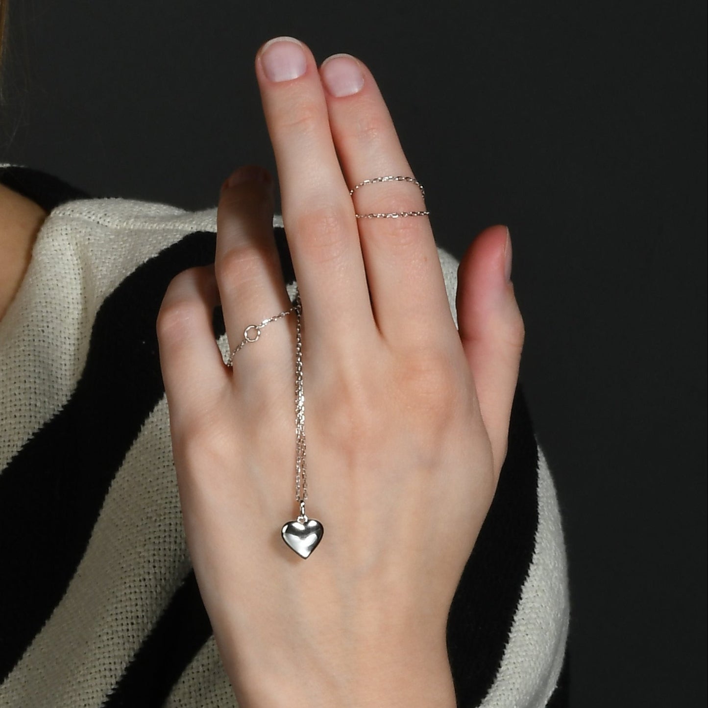 A hand showcasing a sterling silver necklace with a concave heart pendant.