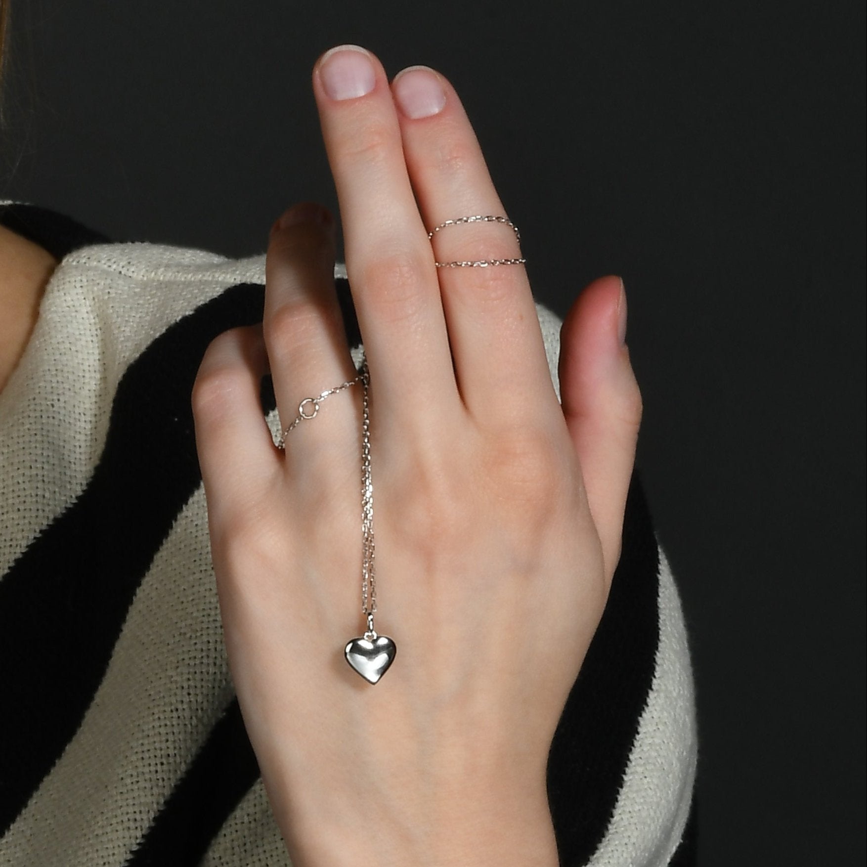 A hand showcasing a sterling silver necklace with a concave heart pendant.