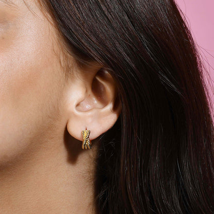 A person wearing a small hoop earring with an intertwined rope design on a pink background.