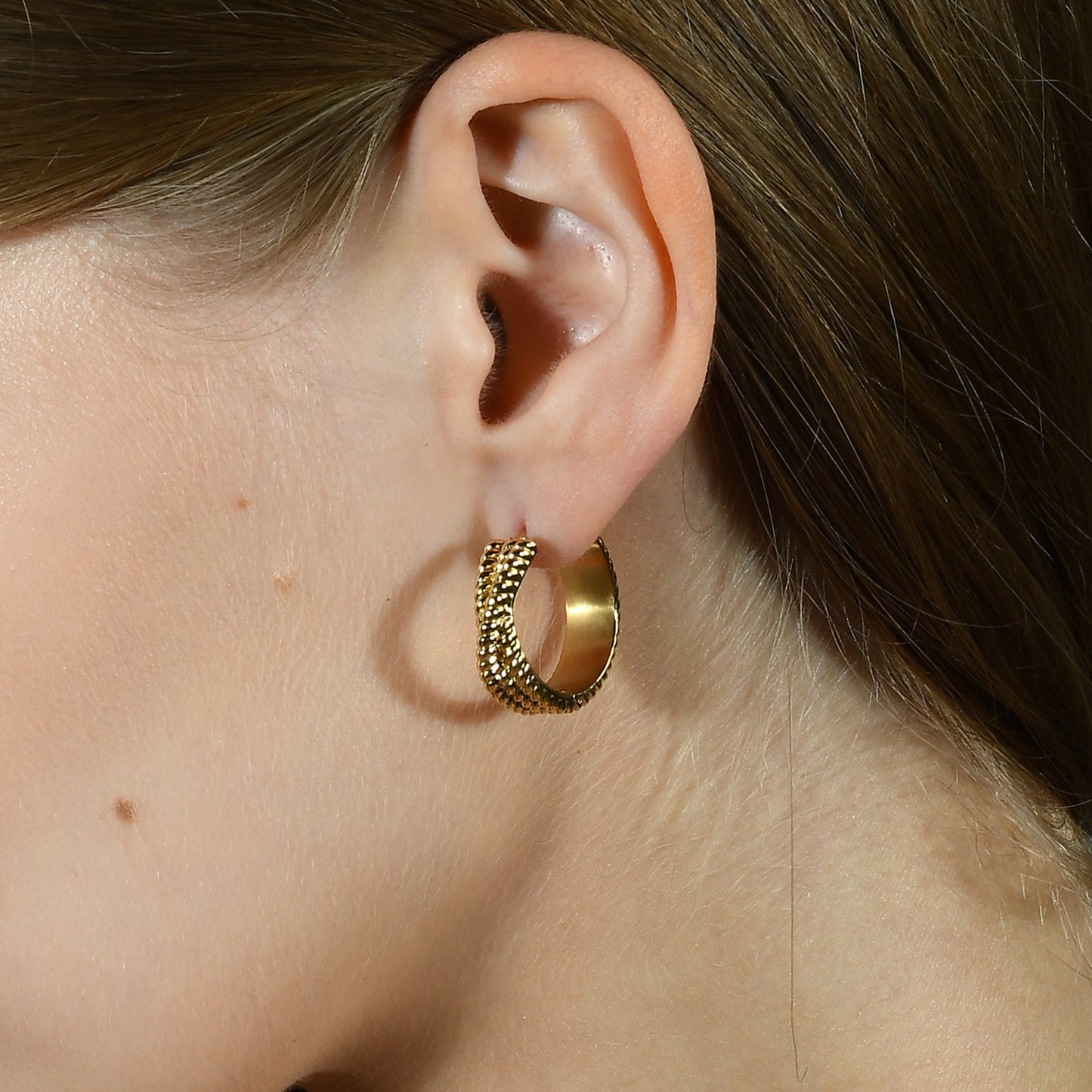 A close-up image of a person wearing a gold-Plated hoop earring with intricate rope-like details.