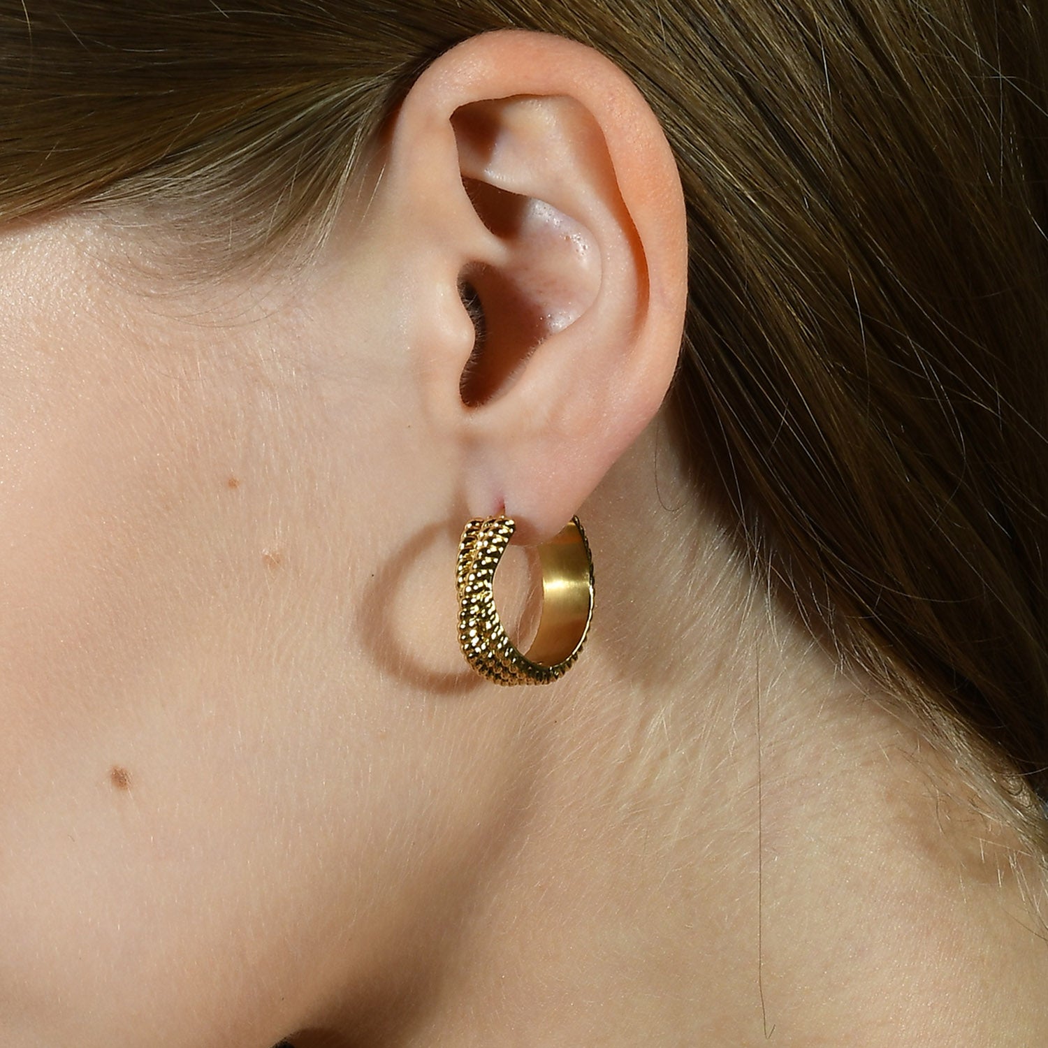A close-up image of a person wearing a gold-Plated hoop earring with intricate rope-like details.