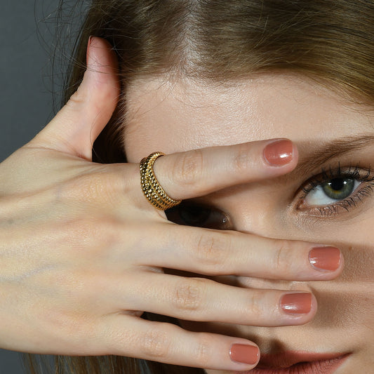 A person's hand with a gold-Plated rope-intertwined ring on their finger, partially covering their face.