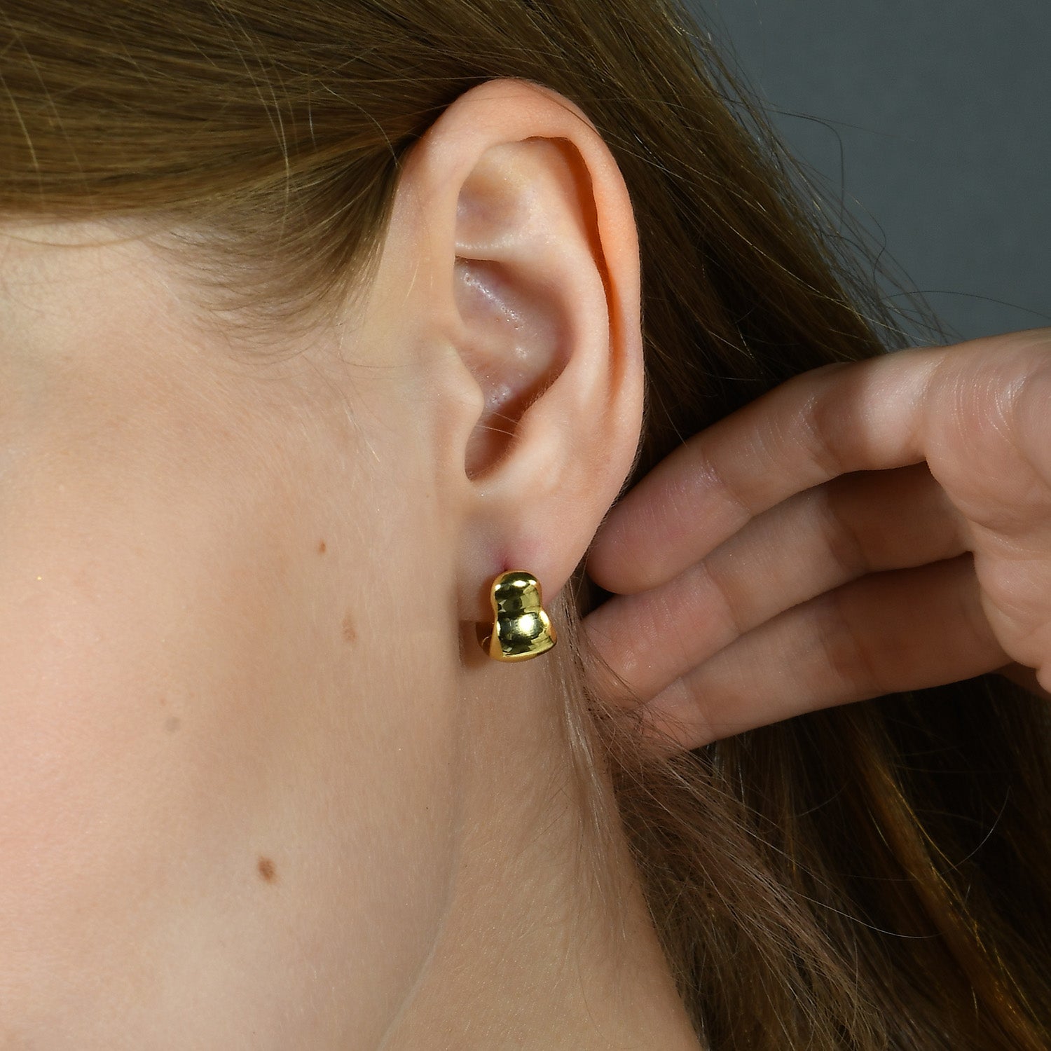 A person wearing a small hoop earring with a gold-colored band.