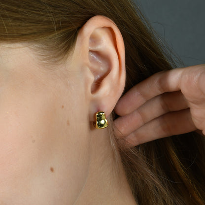 A person wearing a small hoop earring with a gold-colored band.