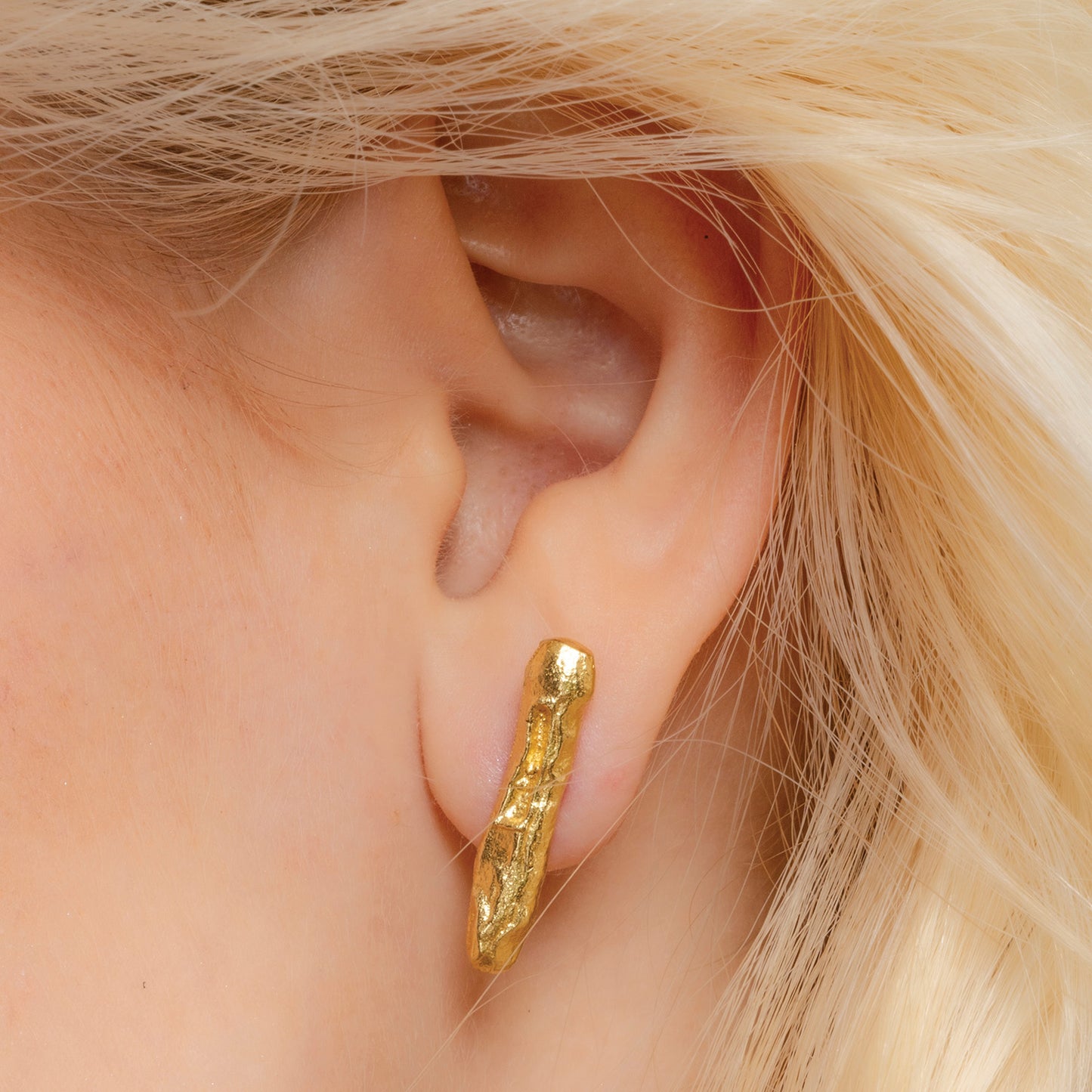 A close-up image of a person's ear wearing a gold-colored monolith stud earring By arvino