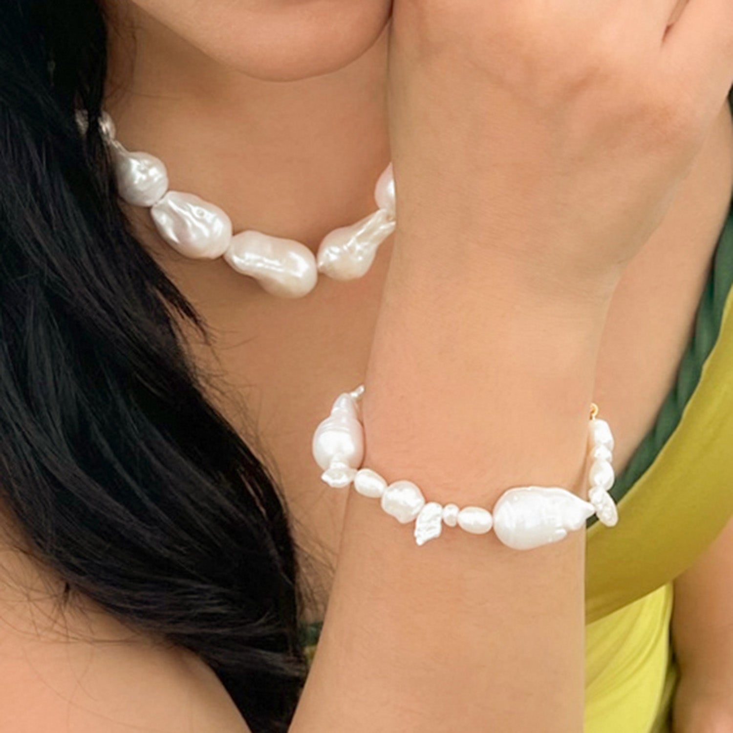 A close-up image of a person wearing a white pearl bracelet with a mix of small and large pearl beads.