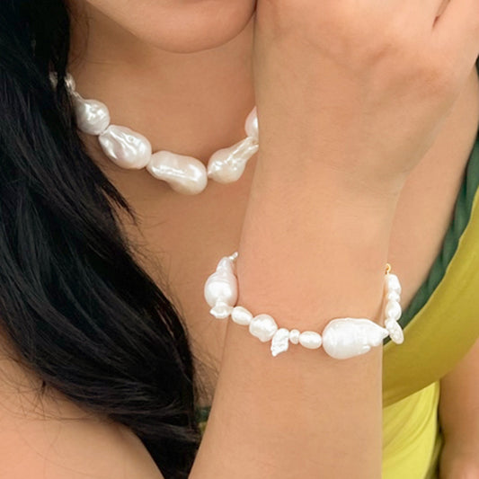 A close-up image of a person wearing a white pearl bracelet with a mix of small and large pearl beads.