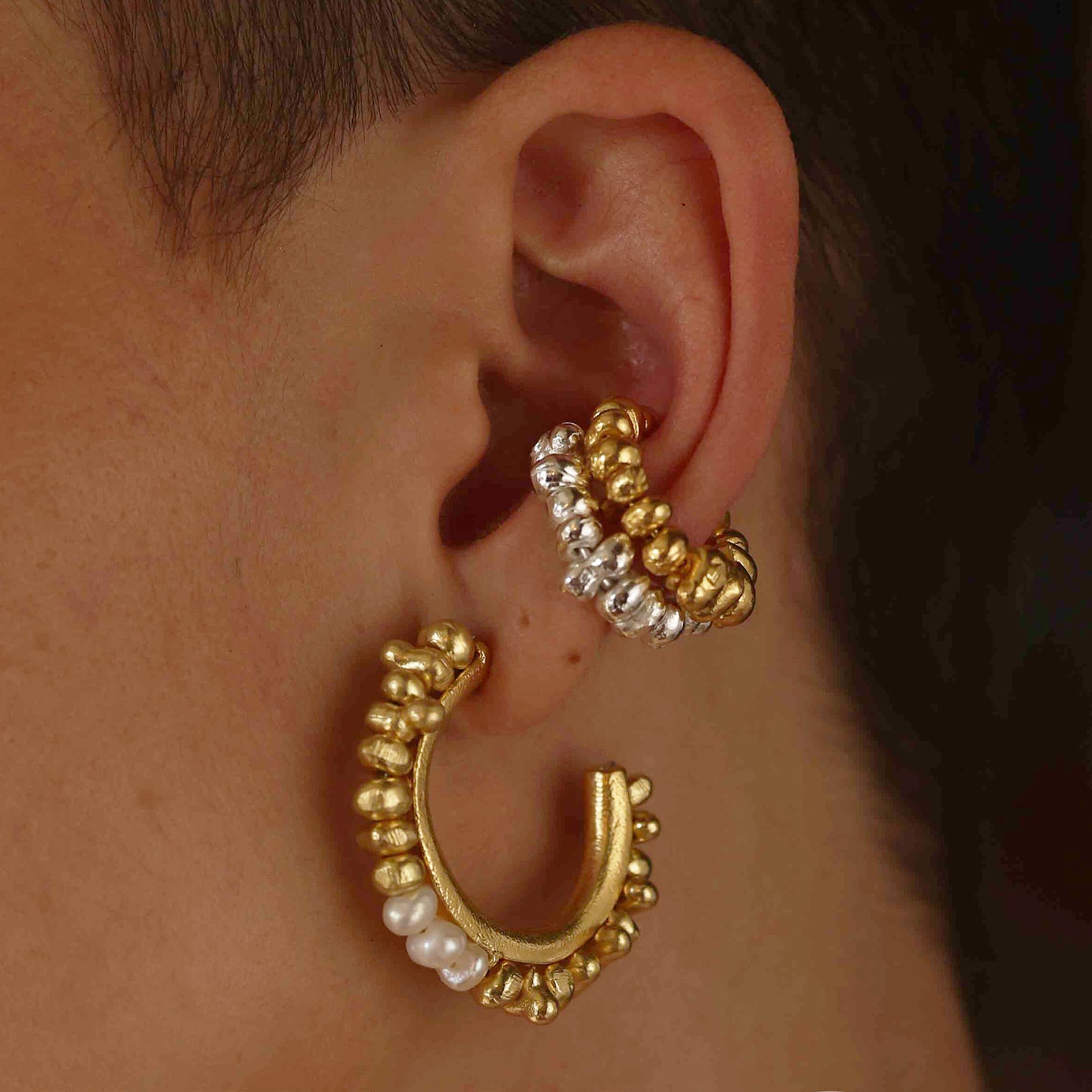 A person wearing a hoop earring with golden-hued metal beads and natural freshwater pearls.