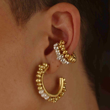 A person wearing a hoop earring with golden-hued metal beads and natural freshwater pearls.