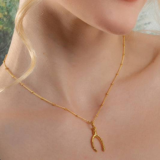 A person wearing a gold-colored necklace with a wishbone-shaped pendant By arvino