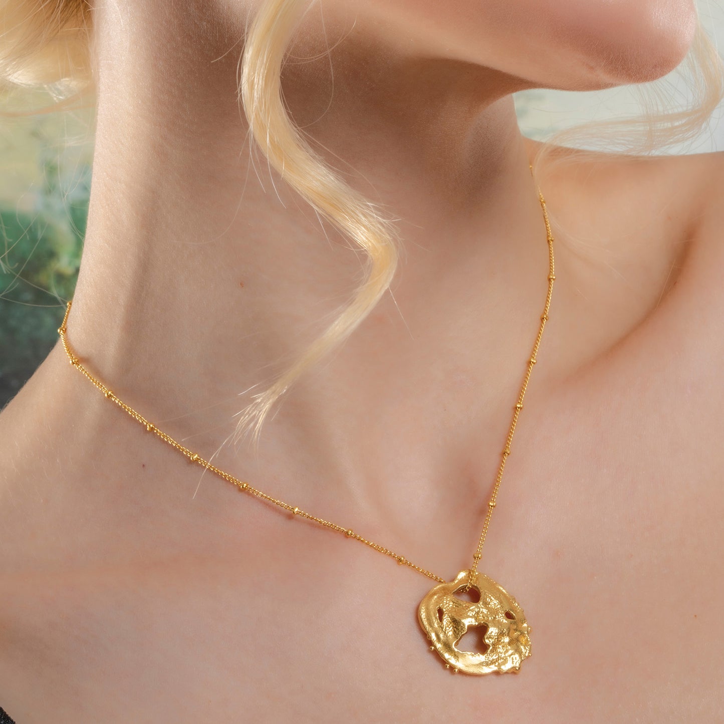 A close-up image of a person wearing a gold-colored necklace with a fossil-like motif pendant.