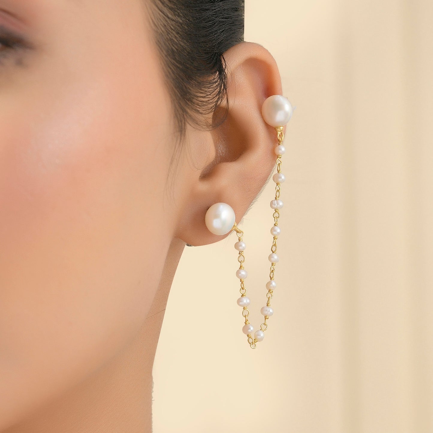 A person wearing a pearl earring with a delicate gold plated chain designed to wrap around the ear.