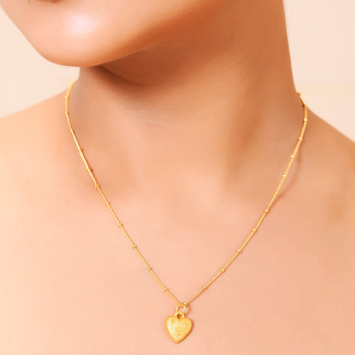 A gold-plated pendant necklace with a heart-shaped pendant and a chain, displayed on model neck