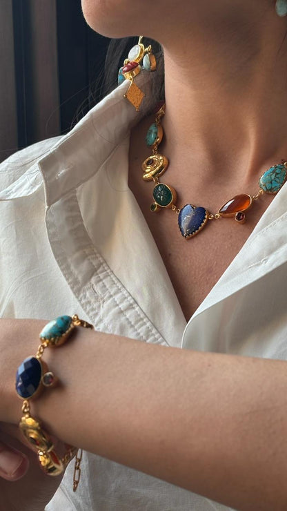 Close-up of a person wearing a colorful gemstone necklace and bracelet on a white shirt.